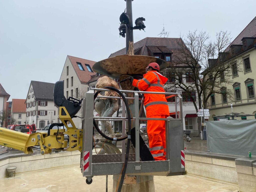 Arbeiter reinigt Brunnen mit Hebebühne.