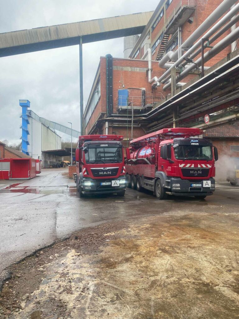 Zwei rote LKWs vor Fabrik.