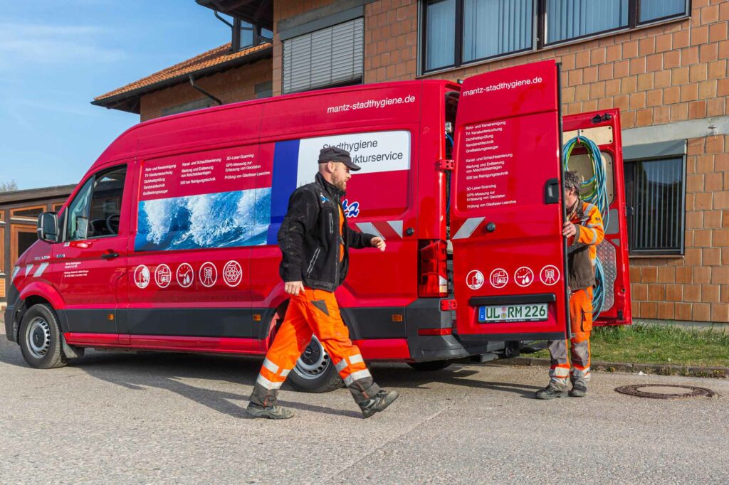Zwei Arbeiter, roter Servicewagen, Schläuche.
