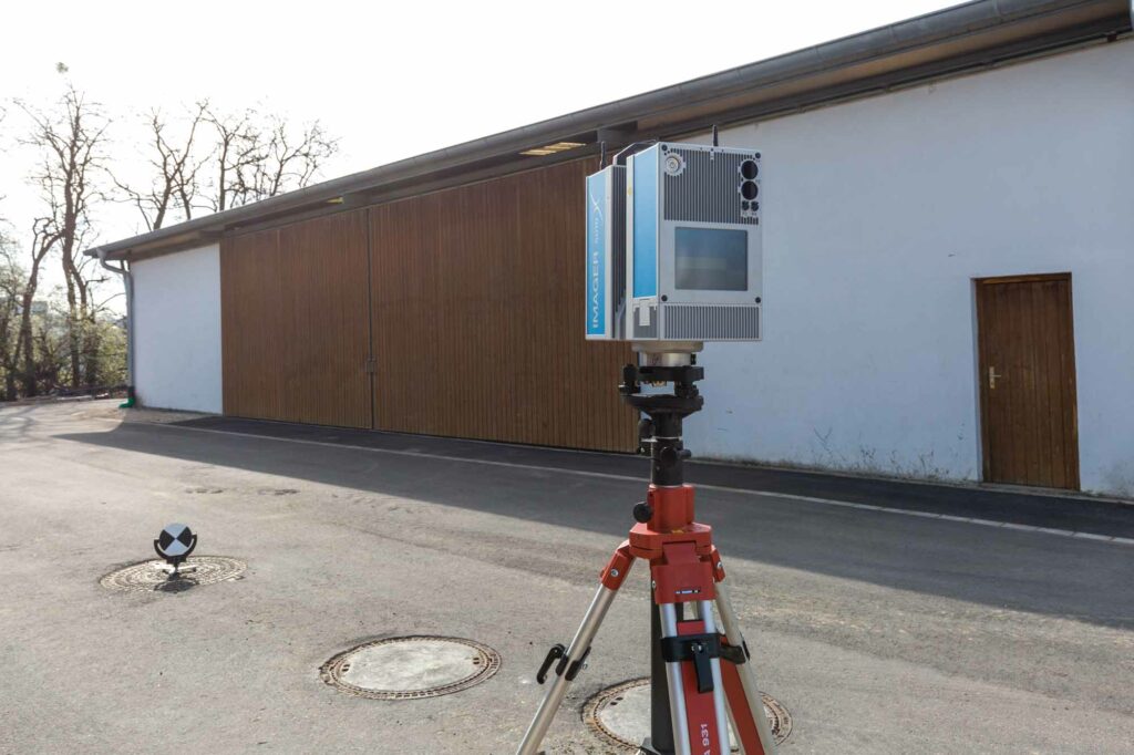 Laserscanner auf Stativ vor Halle.